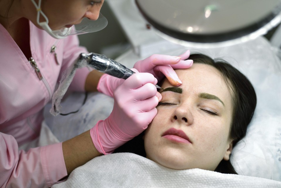 a woman in pink gloves is getting her eyebrows tattooed