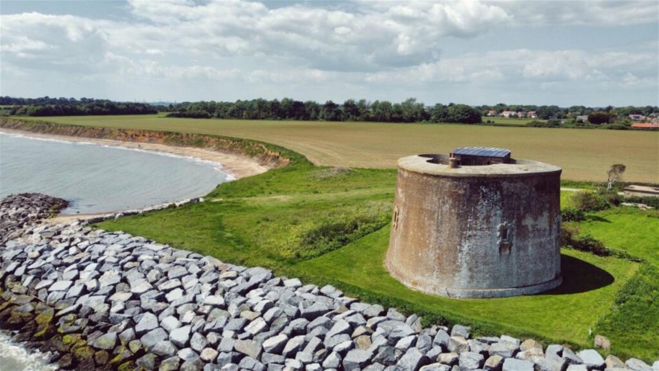 a large stone tower sits on the shore of a body of water