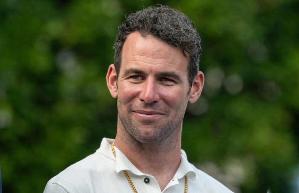 a man wearing a white shirt and a gold chain around his neck smiles