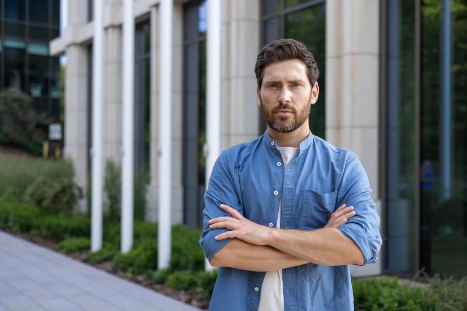 Portrait of a serious and self-confident male businessman, programmer in casual clothes. Standing on the street outside the office center, crossing his arms over his chest and looking at the camera.