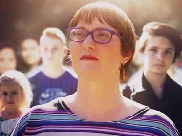 a woman wearing glasses is standing in front of a crowd of people .