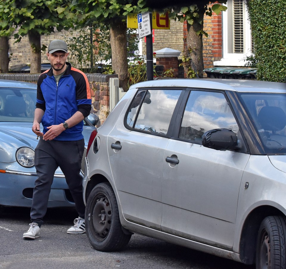 a man in a blue puma jacket stands next to a silver car