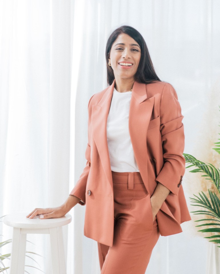 a woman in a suit is leaning against a white stool