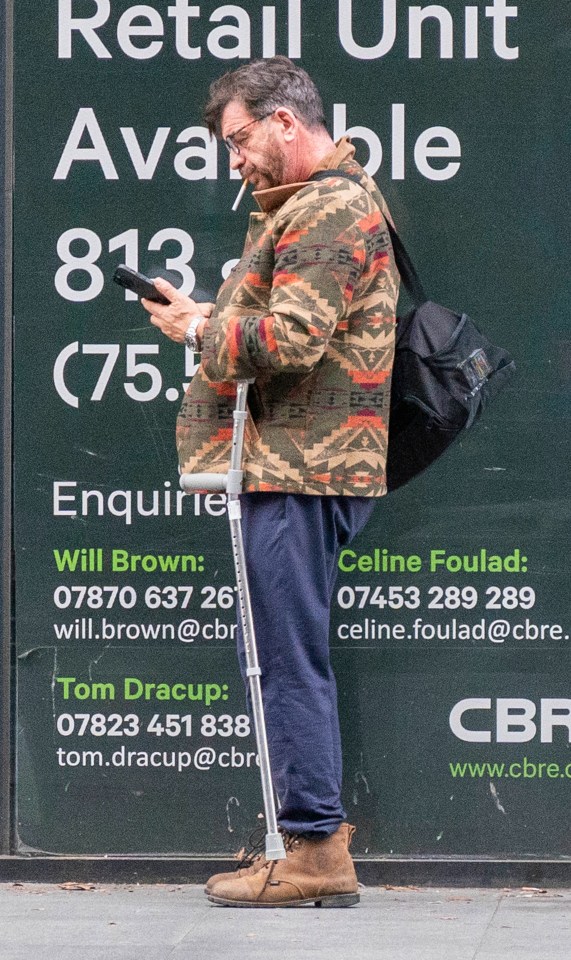 a man with crutches looks at his phone in front of a sign that says retail unit available