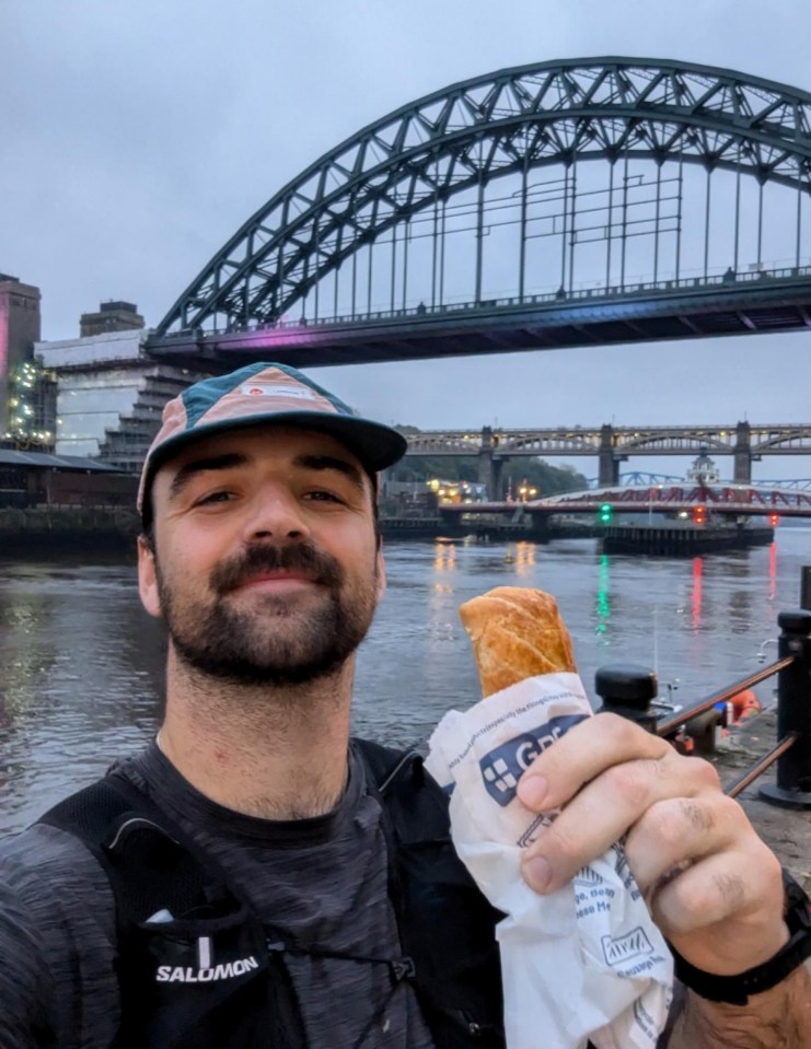 a man wearing a salomon shirt is holding a sandwich in front of a bridge