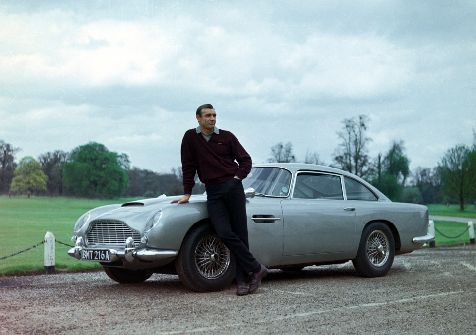 Sean Connery as James Bond posing next to the Aston Martin DB5 in the iconic 1964 Goldfinger