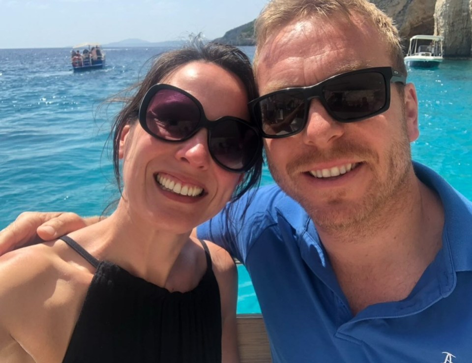 a man and a woman are posing for a picture with a boat in the background