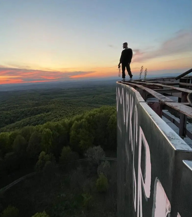 a man stands on the edge of a very tall building with a sunset in the background