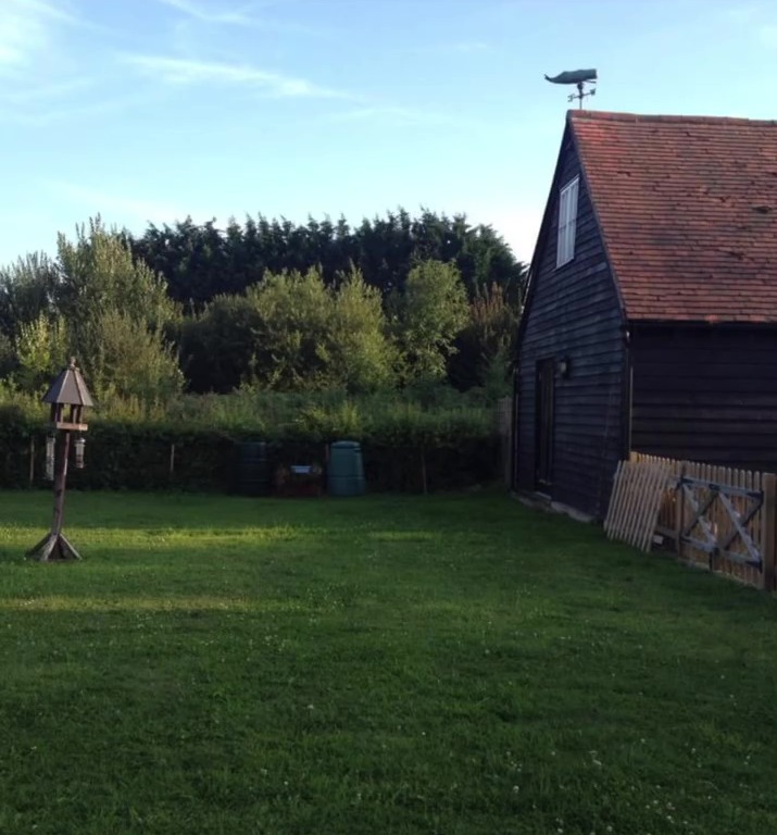 a bird feeder sits in the grass in front of a barn