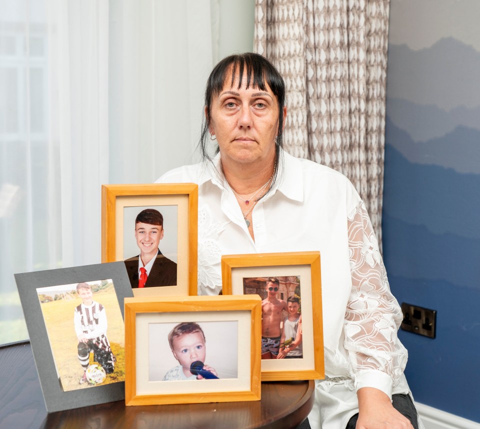 a woman sits at a table holding four framed pictures of her children