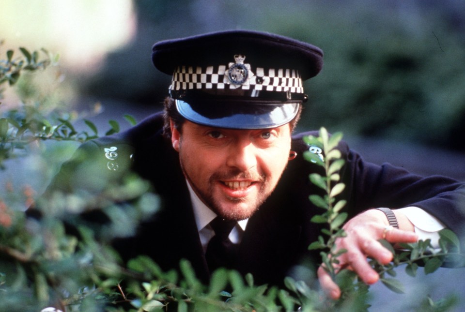 a man in a police uniform is peeking out from behind a bush