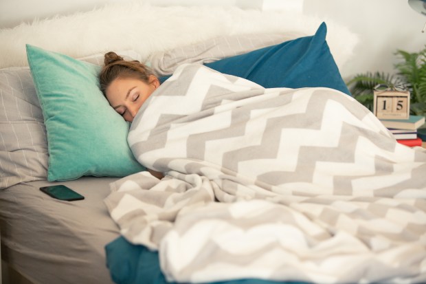 Young woman is sleeping in her cozy bed, covered with warm blanket. Her smart phone is near her.