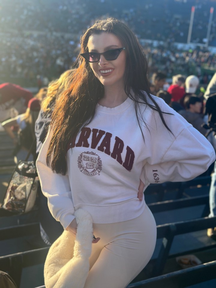 a woman wearing a harvard sweatshirt stands in the stands