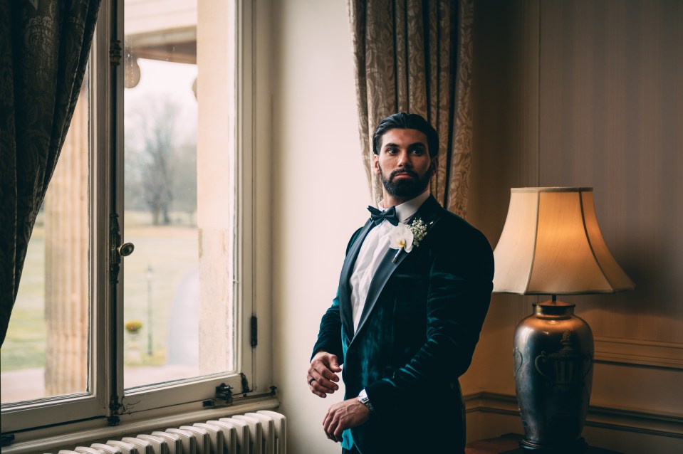 a man in a tuxedo stands in front of a window