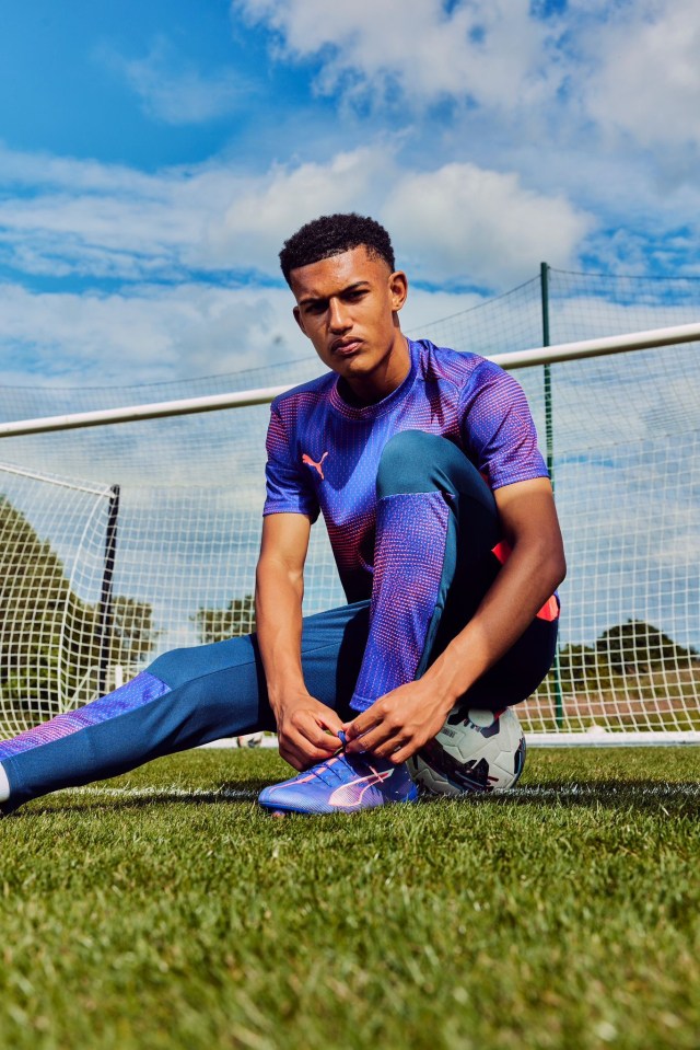 a man in a purple shirt is tying his shoelaces on a soccer field