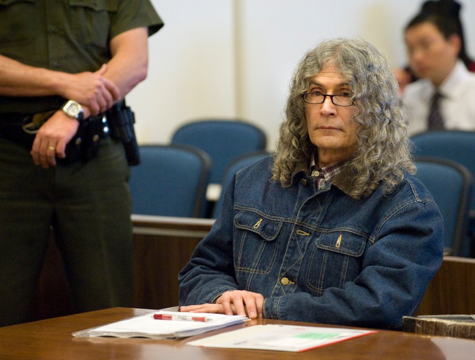 a man in a denim jacket sits at a table in a courtroom