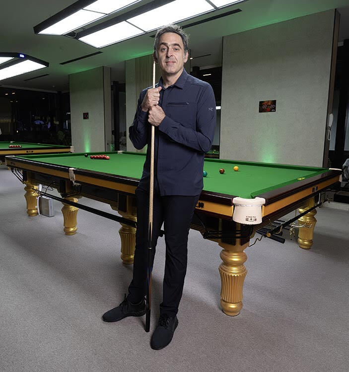 a man stands in front of a pool table holding a cue