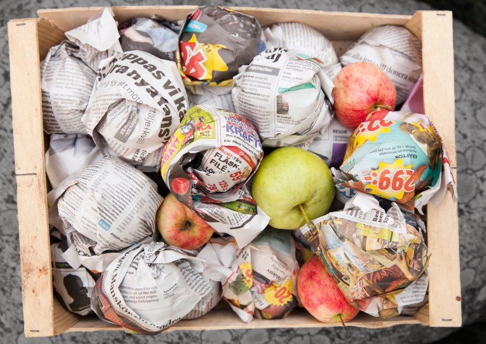 a box of apples wrapped in newspapers including one that says kraft