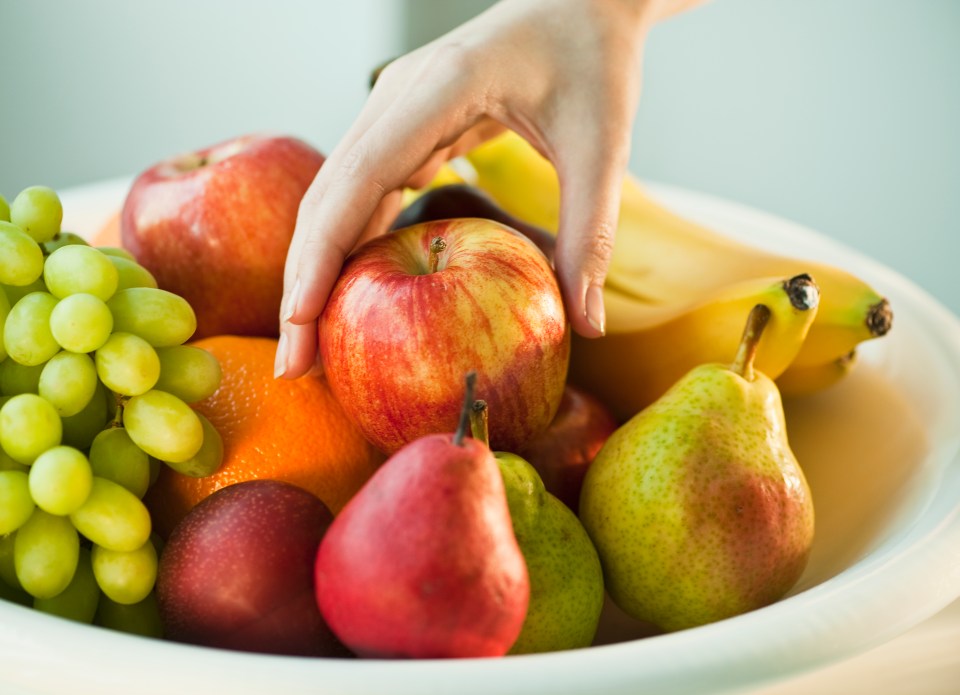 a person reaches for an apple in a bowl of fruit