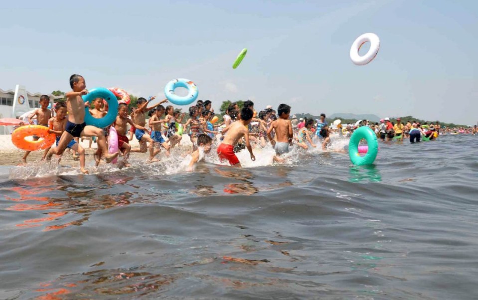 a group of children playing in the water with a green frisbee flying in the air