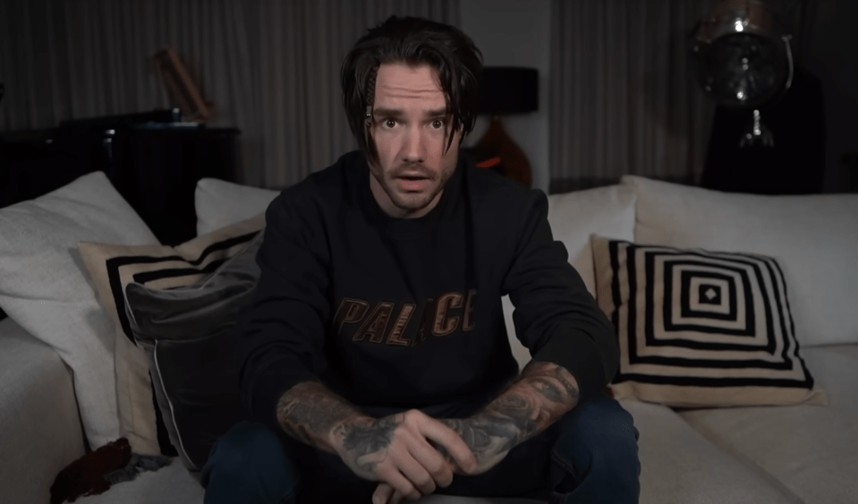 a man wearing a black palace sweatshirt sits on a couch