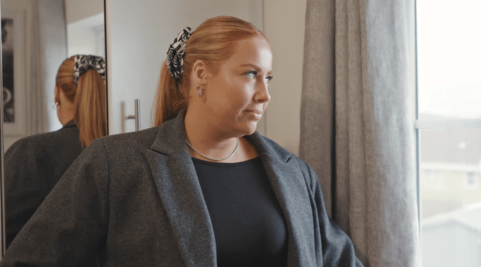 a woman in a gray jacket looks out a window