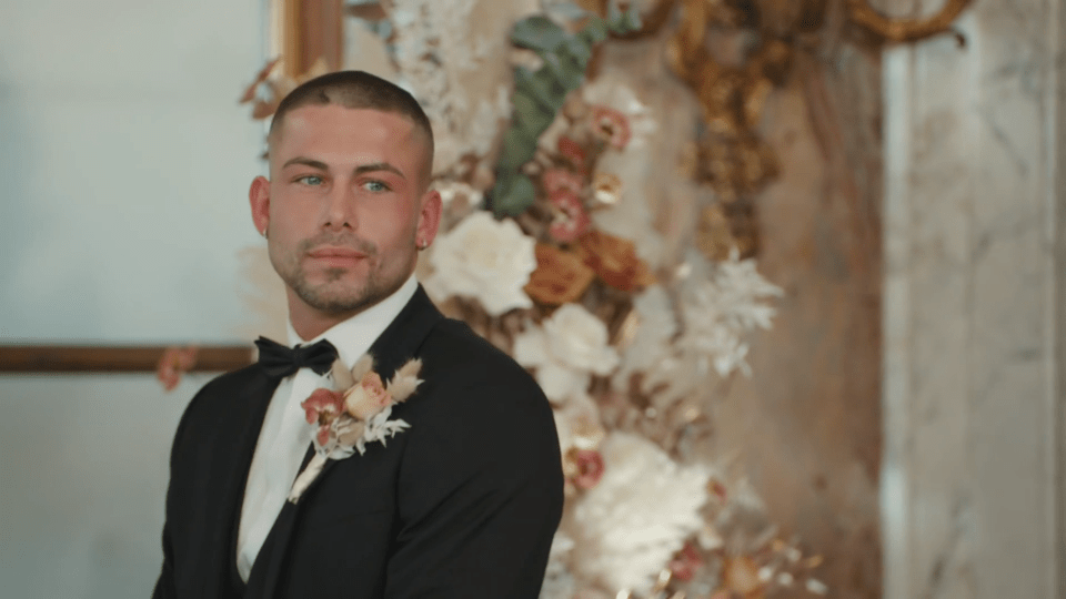 a man in a tuxedo with flowers in the background