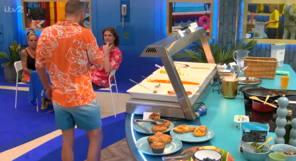 a man in an orange shirt stands in front of a buffet line with itv2 written on the bottom