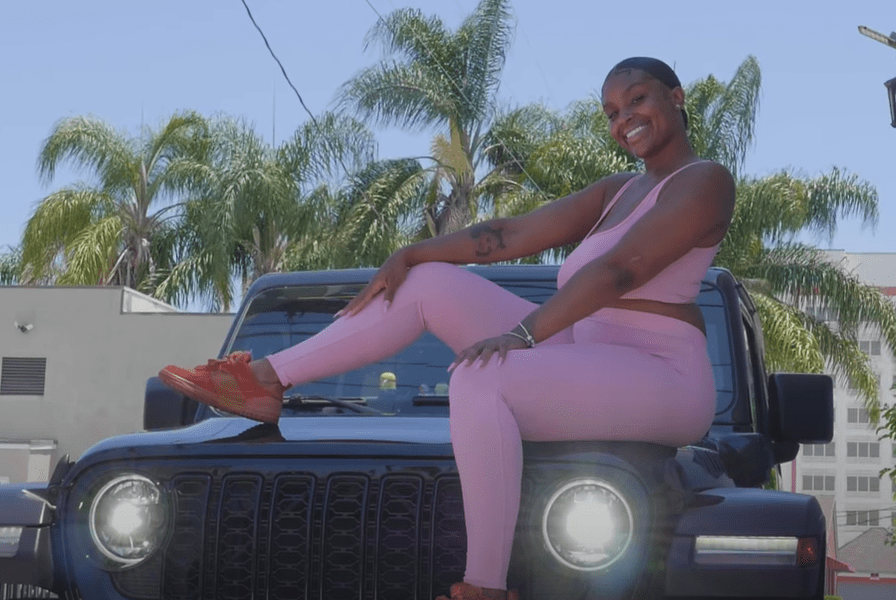 a woman in a pink outfit sits on the front of a black jeep