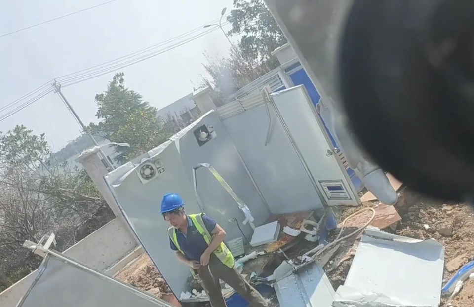 a man wearing a hard hat stands in front of a building that has a fan on it