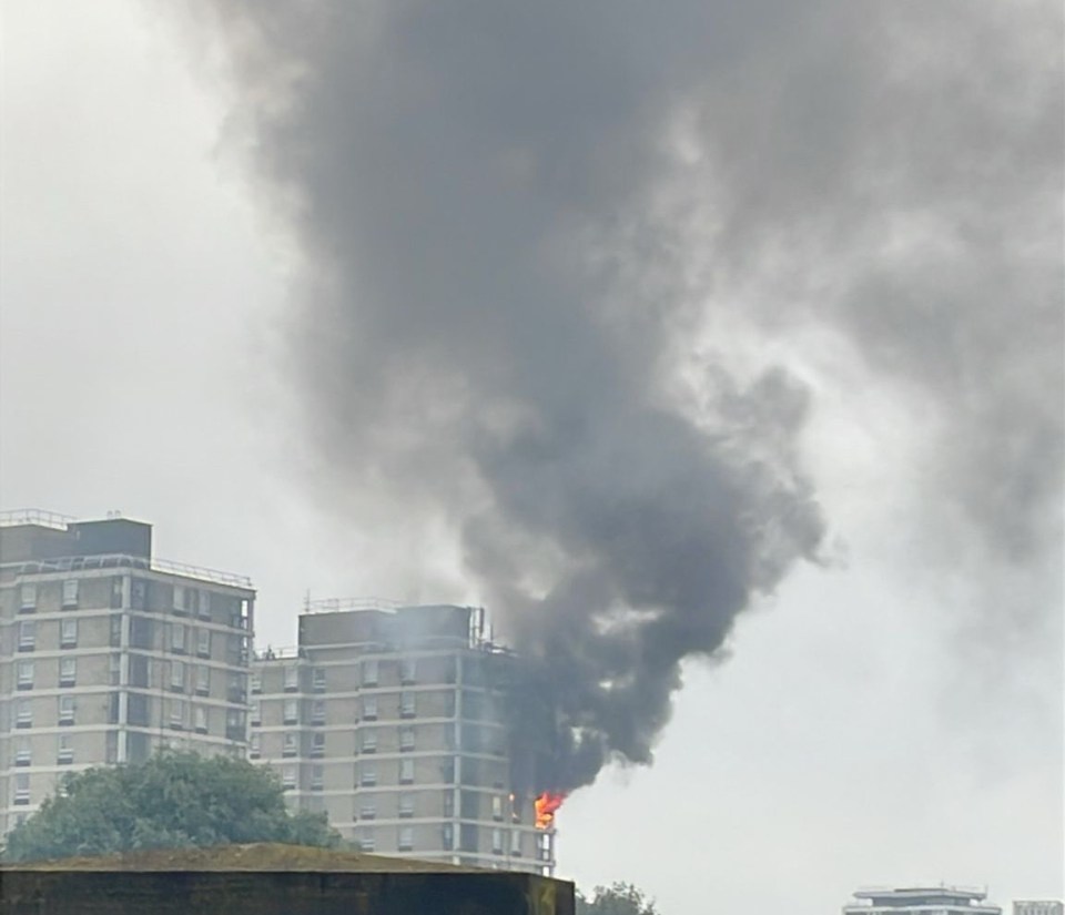 a green sign with a phone on it is in front of a building with smoke coming out of it