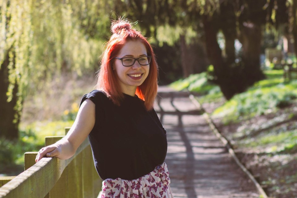 a woman with red hair and glasses leans on a wooden railing