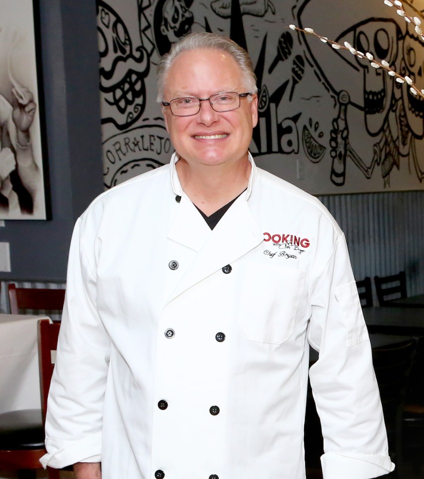 a man in a chef 's uniform stands in front of a table full of food