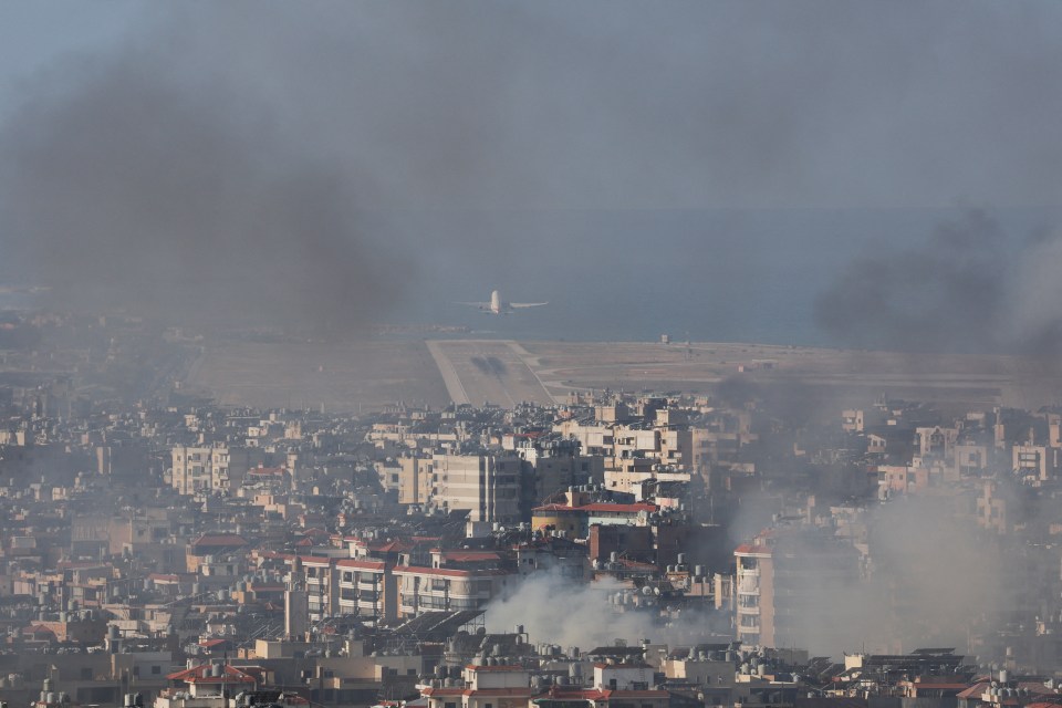 a plane is flying over a city with smoke coming out of it