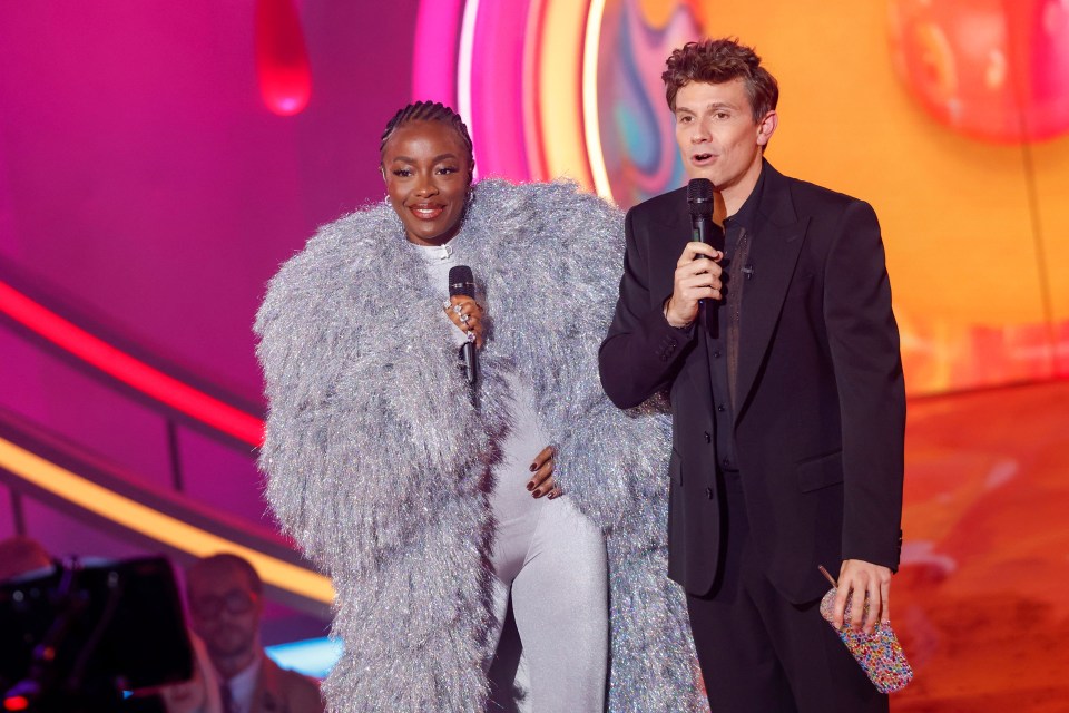 a woman in a fur coat stands next to a man holding a microphone