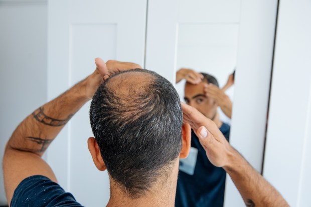 a man with a tattoo on his arm looks at his hair in a mirror