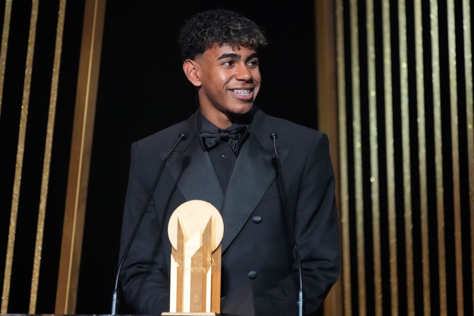 a man in a tuxedo stands at a podium with a trophy in front of him