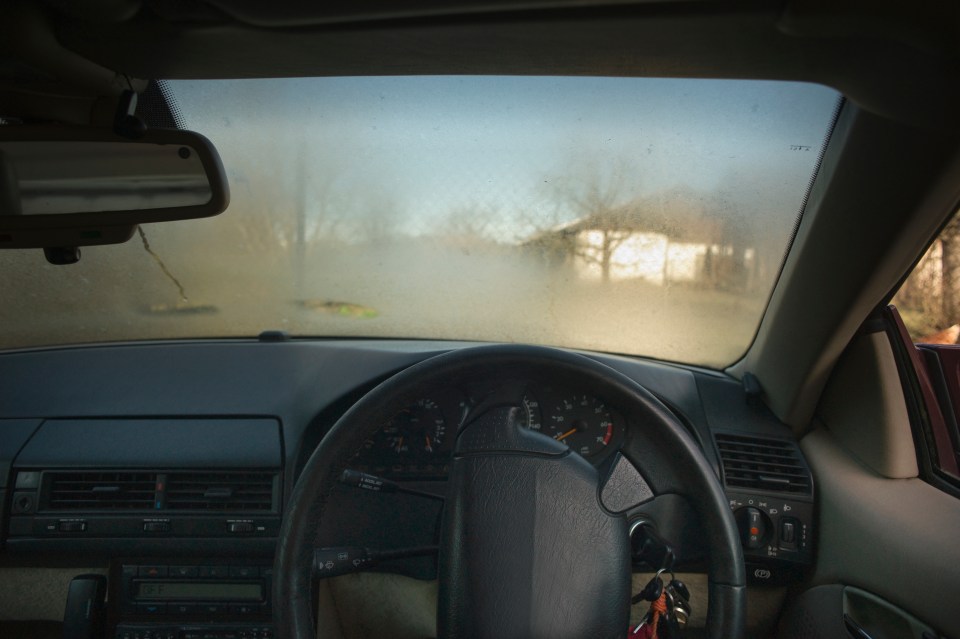 a car 's windshield is foggy and shows a red car in the background