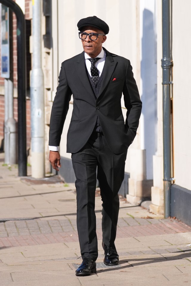 a man in a black suit and black hat walks down a sidewalk