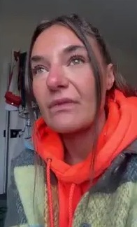 a woman wearing an orange hoodie and a plaid jacket is crying .