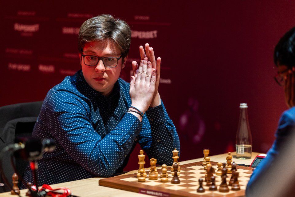 a man playing chess in front of a wall that says superbet