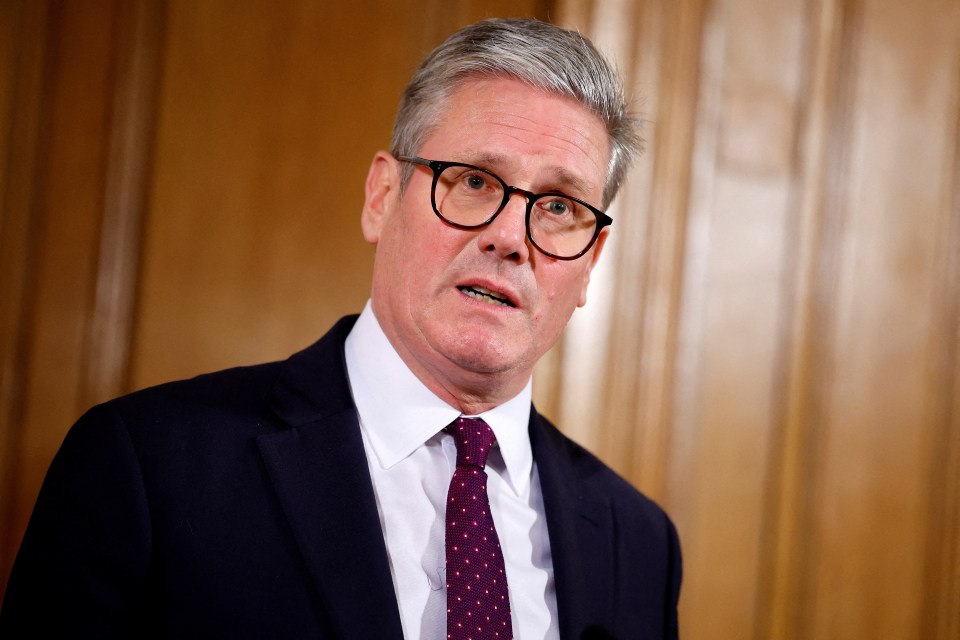 a man wearing glasses and a suit stands in front of a wooden wall