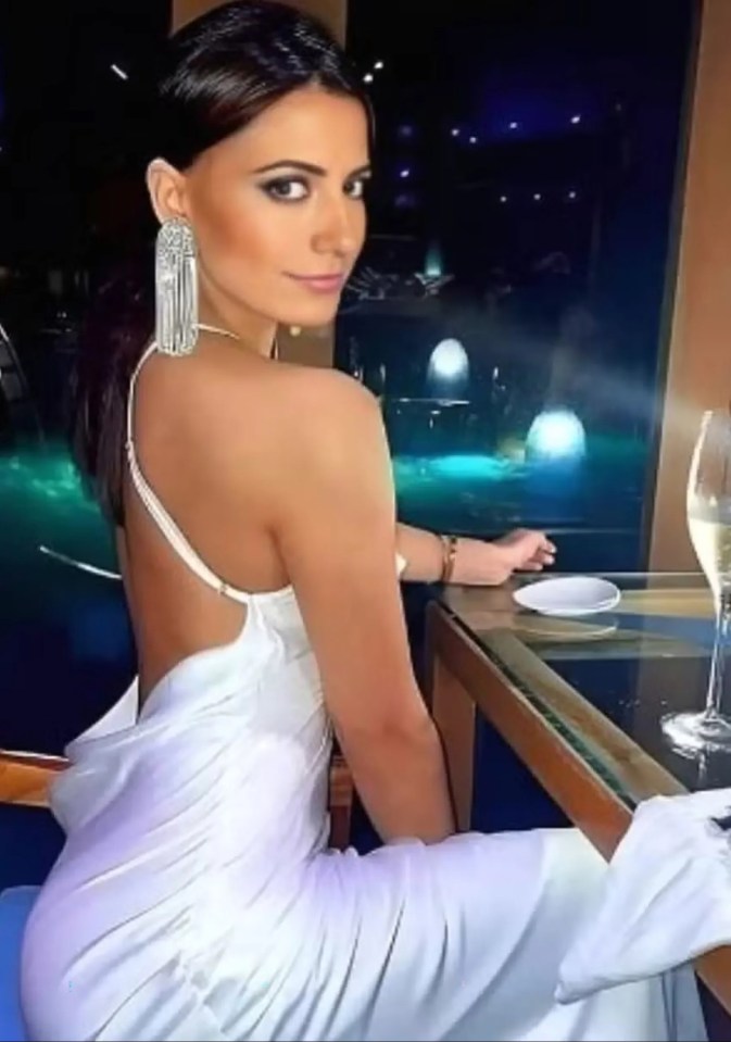 a woman in a white dress is sitting at a table with a glass of wine .