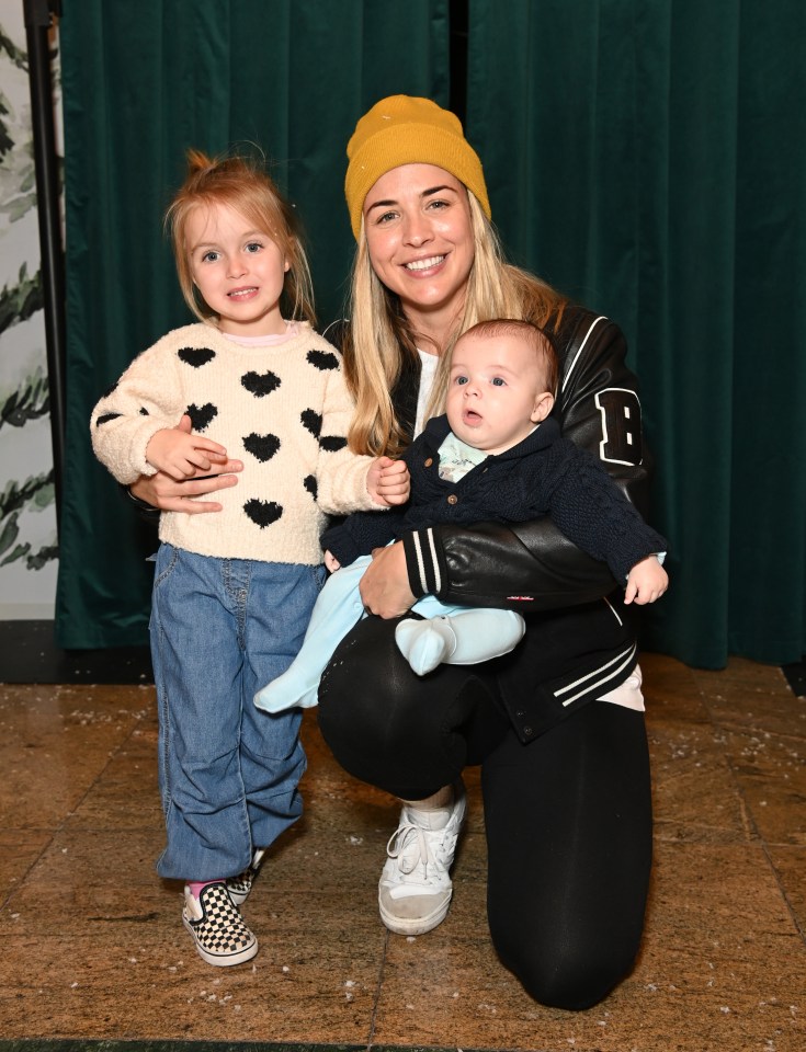 a woman is kneeling down holding a baby and wearing a jacket with the letter b on it