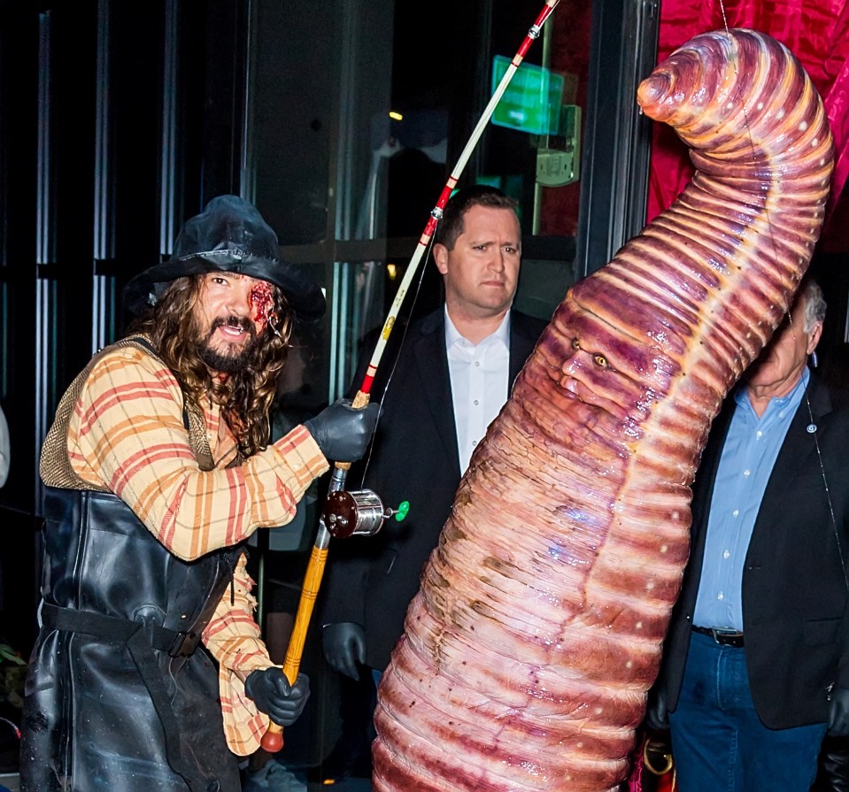 a man in a costume is holding a fishing rod next to a large worm