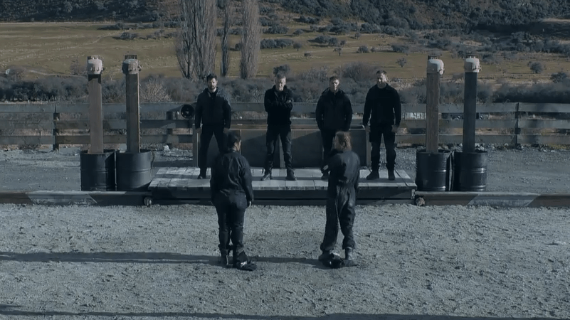 a group of people standing in front of a fence with barrels and a sign that says ' a ' on it