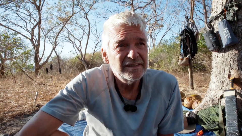 a man sits on a blue tarp next to a tree with a water bottle that says columbia on it