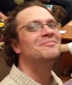 a man wearing glasses is smiling for the camera while sitting at a table .