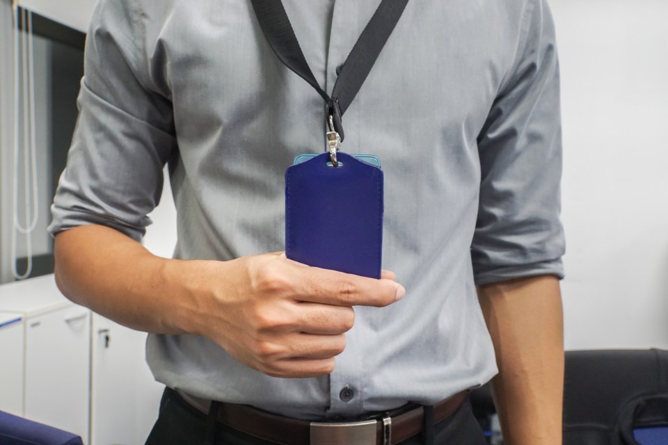 a man in a grey shirt is holding a blue lanyard around his neck