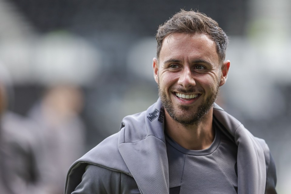 a man with a beard is smiling and wearing a grey adidas jacket